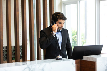 Handsome male receptionist is talking to a tourist who is making a online booking over the phone