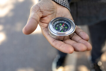 Male traveler holding a magnetic compass on asphalt road, orientation and finding your way.