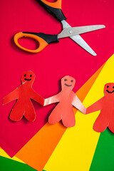 Figures of people made of paper, holding hands. Origami from colored paper.  Gays, lesbians, transgender people, homosexuals on the background of colored paper in the color of the lgbt flag.