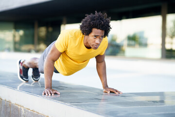 Fototapeta premium Black man doing triceps dip exercise on city street bench.