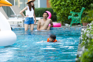 Asian little boy and family swiming in swimming pool at park. Family Leisure and travel at holidays...