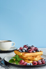 Vanilla Belgian waffles with berries and a cup of coffee for breakfast.