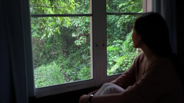 Blurred of a young woman sitting in the house and looking at a beautiful nature outside the window