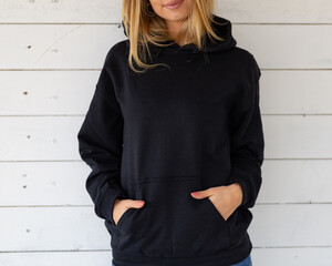 Sweatshirt hoodie mockup. Unrecognizable woman stands in a black sweatshirt against a background of white boards, facing the camera. - 440534689