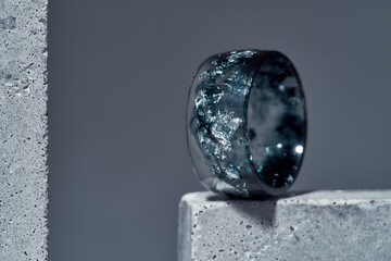 Close up of stylish ring made of dark blue epoxy resin with silver foil inside on concrete element isolated over gray background - obrazy, fototapety, plakaty