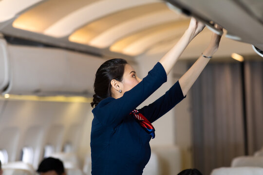 Flight Attendant Helping Passenger Put Luggage To Cabin Or Compartment On Airplane