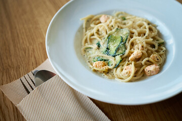Plate of Italian pasta fettuccine in a creamy sauce with salmon and zucchini on a table