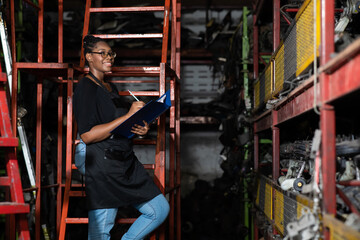 Obraz na płótnie Canvas Plus size black female worker inspecting old car parts stock while working in automobile large warehouse