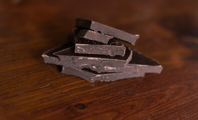 Broken pieces of dark chocolate on a wooden brown background.