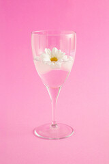 Summer composition with a glass of drink, flowers and ice against a pastel pink background. Minimal party and drink concept.