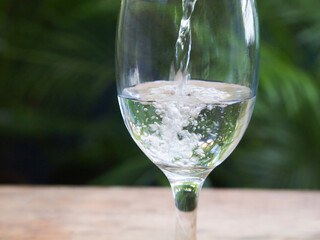 Pouring water in to a glass on a wooden table against natural background. 
