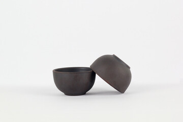 A Chinese black ceramic teapot and teacup isolated on a white background.