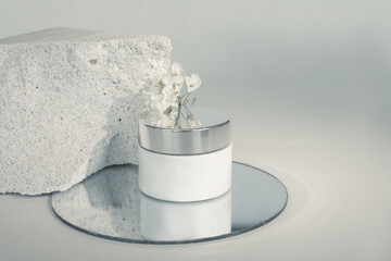 cream box on piece of concrete in cut. The porous structure of concrete is associated with texture of human skin. Composition uses amirror and delicate flower. Medical cosmetics concept