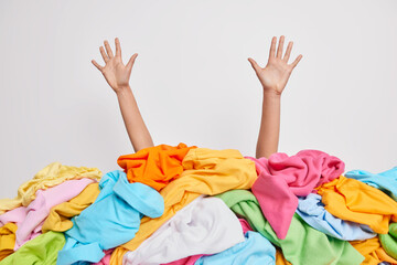 Human hands reaching out from big pile of colorful unfolded clothes against white studio background. Heap of laundry after washing. Cluttered wardrobe. Used clothing for donation and recycling - 440539033
