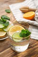 Glass of healthy lemonade and citrus fruits on wooden background