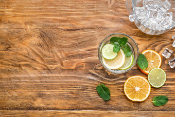 Fototapeta na wymiar Glass of healthy lemonade, ice cubes and citrus fruits on wooden background