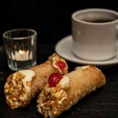 Close-up of cannoli on black stone slab with cup of coffee in the background.
