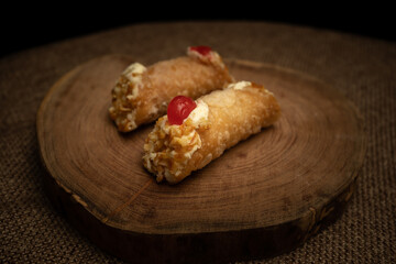 Close-up of two cannoli on wooden slice and burlap cloth.