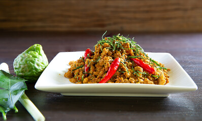 Spicy stir fry minced pork with curry paste (Thai call *Kua kling*) on dark brown wooden table