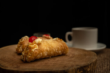 Close-up of two cannoli on wooden slice and burlap cloth. Coffee cup behind.
