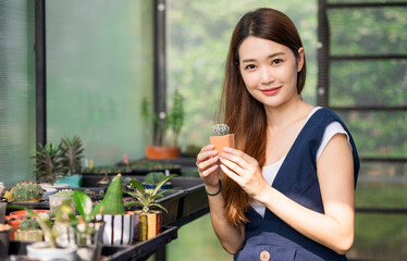 Asian woman Gardener working in houseplant. Owner start up small business  greenhouse. Cute Female holding small tree in pot and smiling in houseplant stay at home.