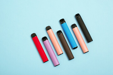 Layout of colorful disposable electronic cigarettes on a blue background. The concept of modern...