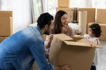 Cute daughter with parent are holding large paper box. Happy family in living room. Moving new house a lot of parcel. Father mother and daughter relax together at new home.