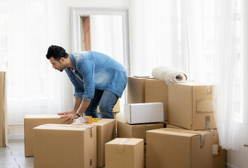 Young man just moving new house. He unpacking parcel box and arranging on the floor in the living room.