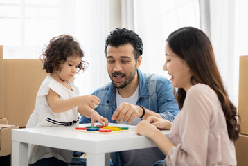 Parents and daughters play with wooden blocks sitting on the floor in the living room at home. The family just moved to a new house. Happy moment Multi-ethnic dad mom and child.