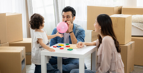 Parents and daughters play with pink balloon sitting on the floor in the living room at home. The family just moved to a new house. Happy moment Multi-ethnic dad mom and child.