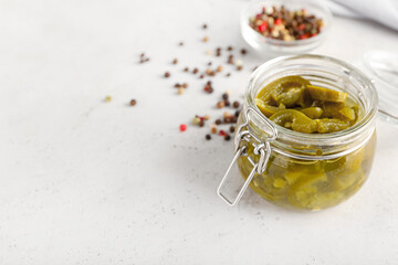 Glass jar with canned jalapeno on light background