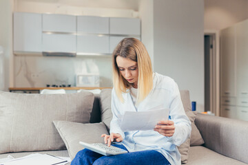 Obraz premium Worried housewife pays inflated bills while sitting on sofa at home, frustrated with work, and monthly income