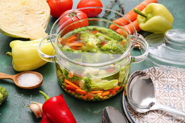Stylish cooking pot with tasty soup and ingredients on color background