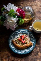 Tea party table - green tea, strawberry crumb cake and a bouquet of summer flowers on a wooden background, top view
