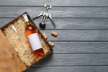 Box with bottle of wine and corkscrew on wooden background