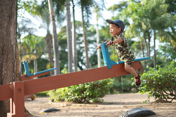 Asian boy in military suit playing and having fun with seesaw