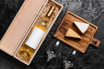 Box with bottle of wine, cheese and glasses on dark background