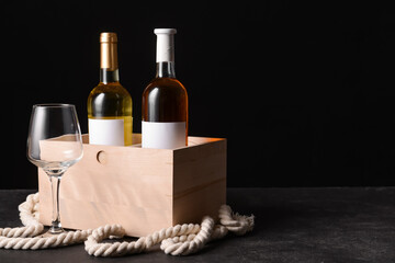 Box with bottles of wine and glass on dark background