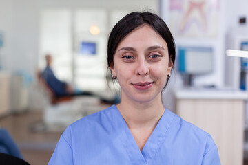 Smiling stomatology nurse looking at camera in dentist office wainting area, senior man waiting for teeth health examination. Dentistiry woman sitting on chair.