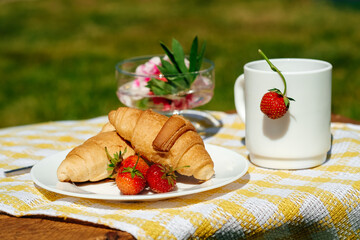 Breakfast table in the garden. Tea with strawberries and croissants.