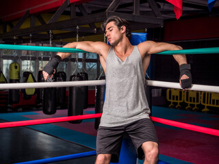Young male boxer resting against boxe ring ropes