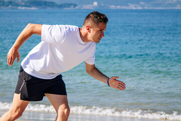 young man in starting position for jogging on the beach