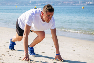 young man in starting position for jogging on the beach