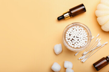 Glass with cotton swabs, balls bottles of cosmetic product on color background