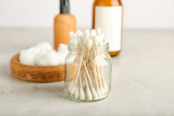 Fototapeta na wymiar Cotton swabs, balls and bottles of cosmetic product on light background