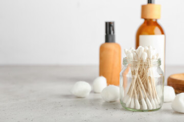 Cotton swabs, balls and bottles of cosmetic product on light background