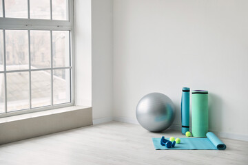 Set of sports equipment with fitness ball near light wall