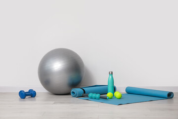 Set of sports equipment with fitness ball near light wall