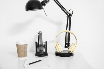 Modern headphones with lamp, cup of coffee and stationery on table in room