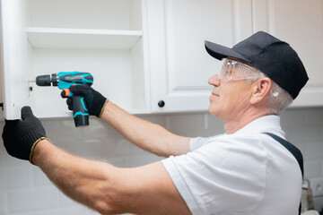 Worker man in uniform installs fittings assembling furniture in kitchen